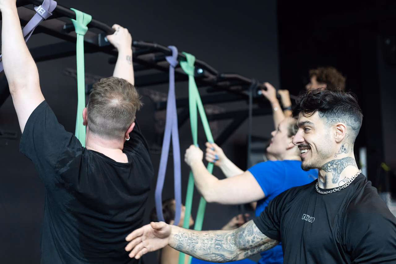 MXO coach supporting participants during band-assisted pull-ups
